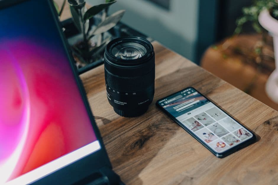 A camera lens beside a smartphone on a wooden desk