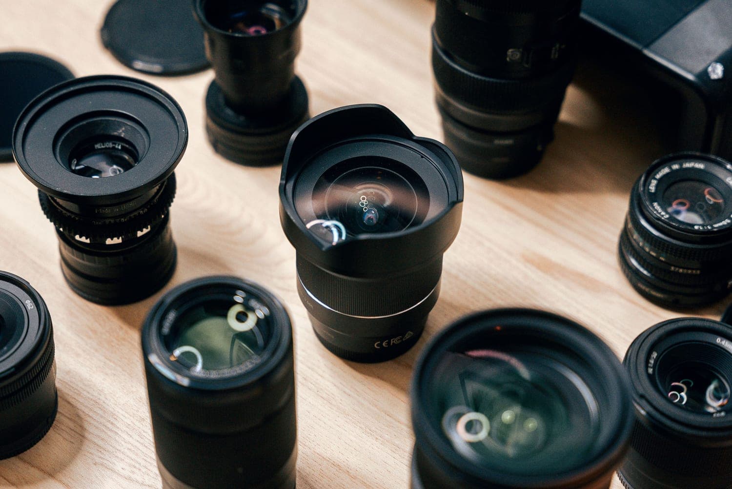 A mirrorless camera and prime lenses on a warm wooden table in golden-hour light