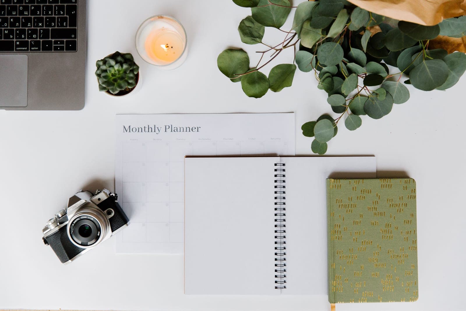 A notebook, a camera and lenses arranged on a desk as if planning a purchase